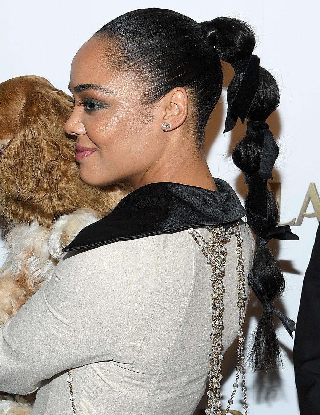 Tessa Thompson wearing a nude outfit with black collar and a bubble ponytail hairstyle with a black bow on each bubble