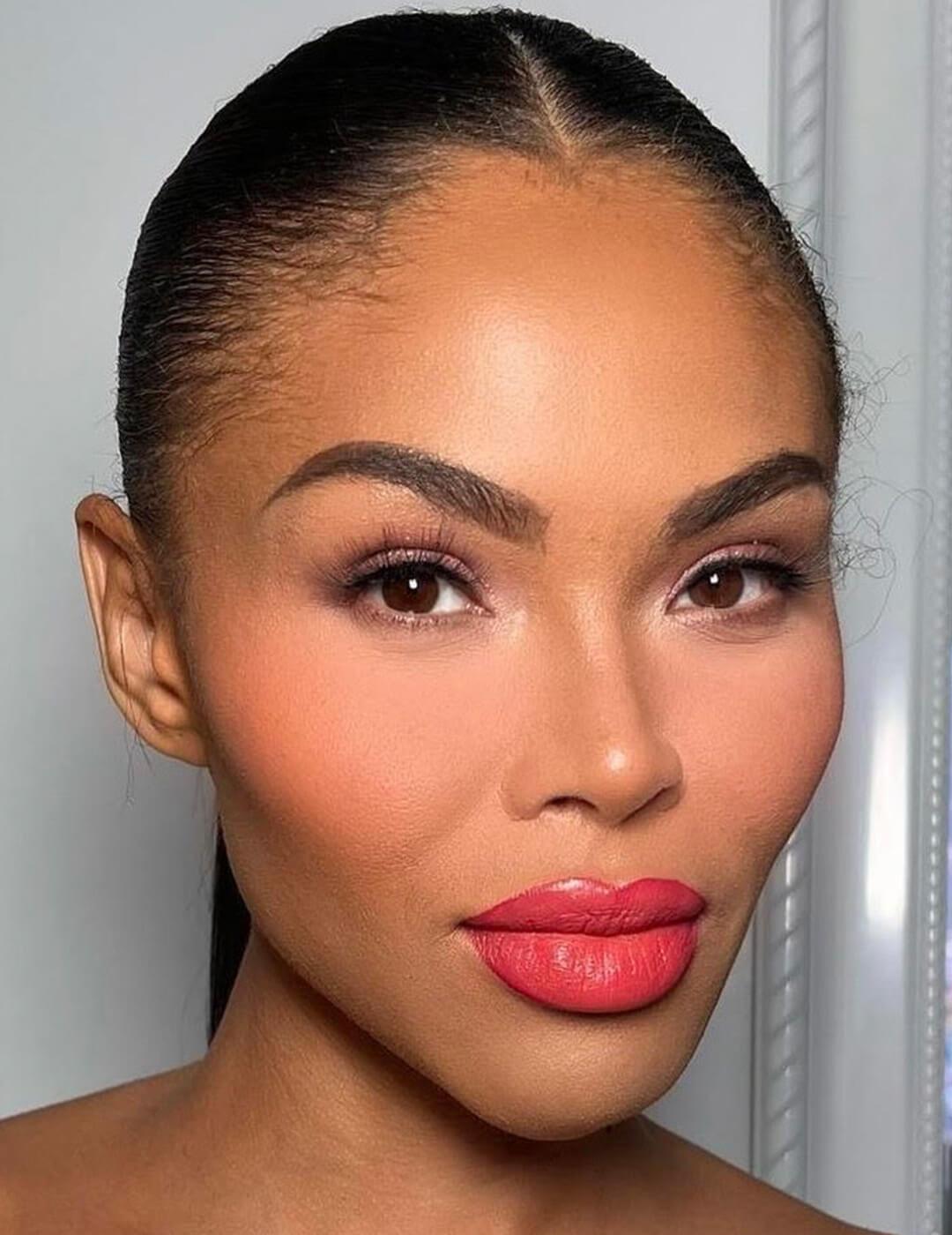 A closeup photo of a model wearing peach blush and pink-peach colored lipstick look