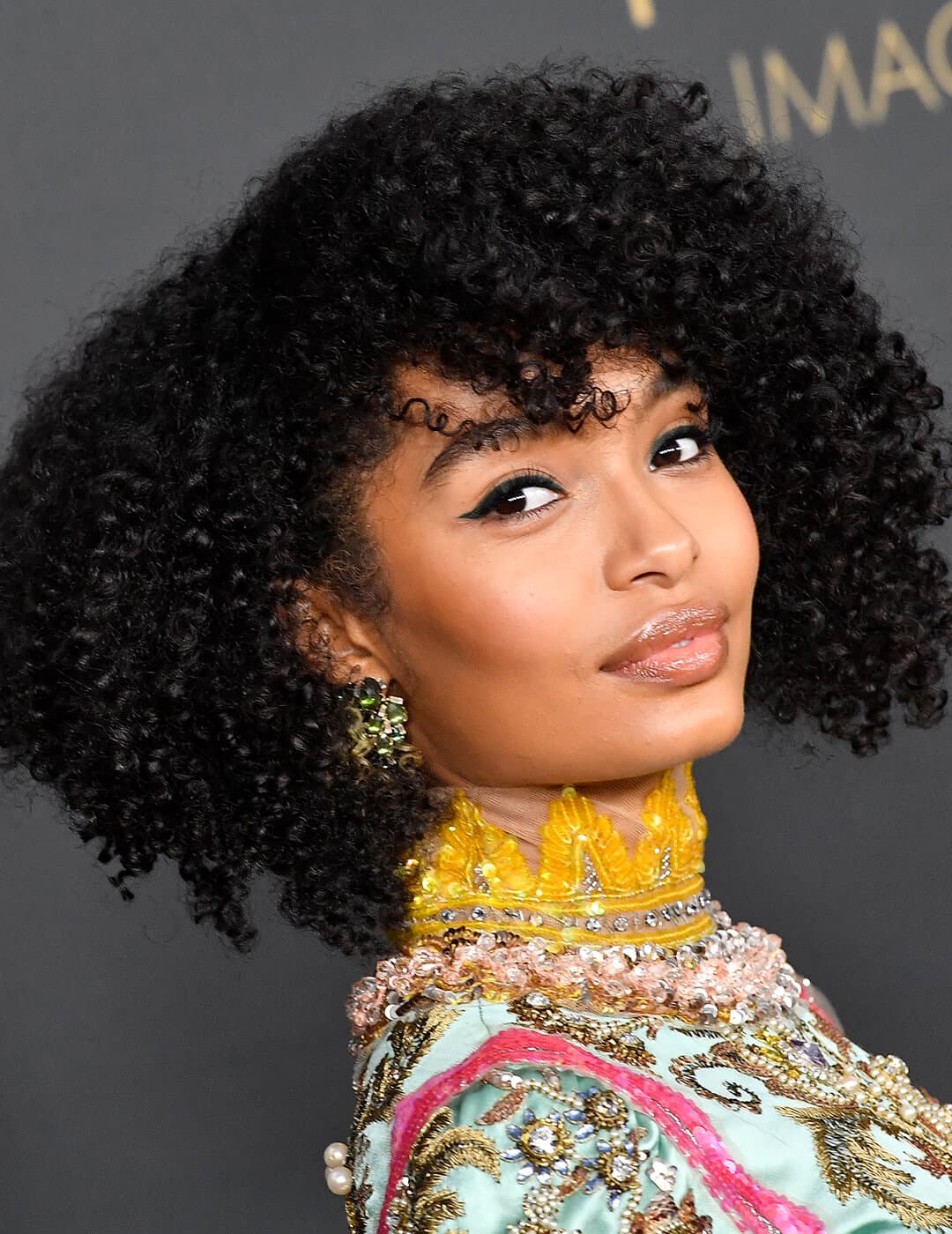 A photo of Yara Shahidi looking fabulous in her curly black bob hair with winged liner on a black background