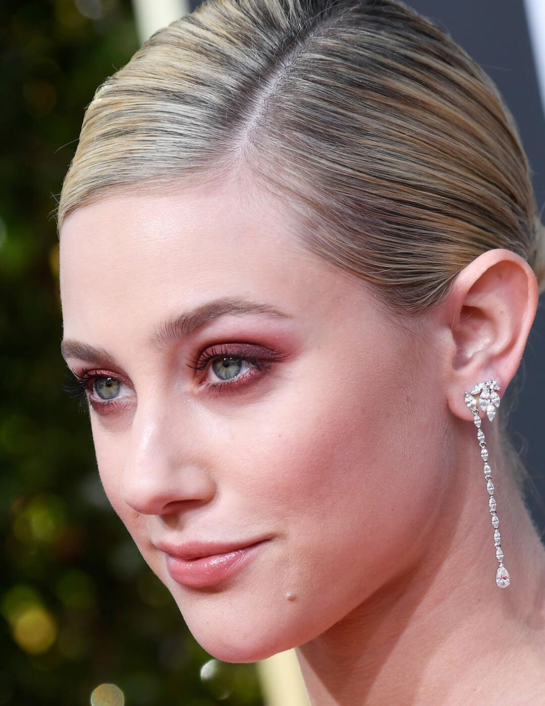 An image of Lili Reinhart showing her red semi-smokey eyeshadow accentuated with her long silver earrings