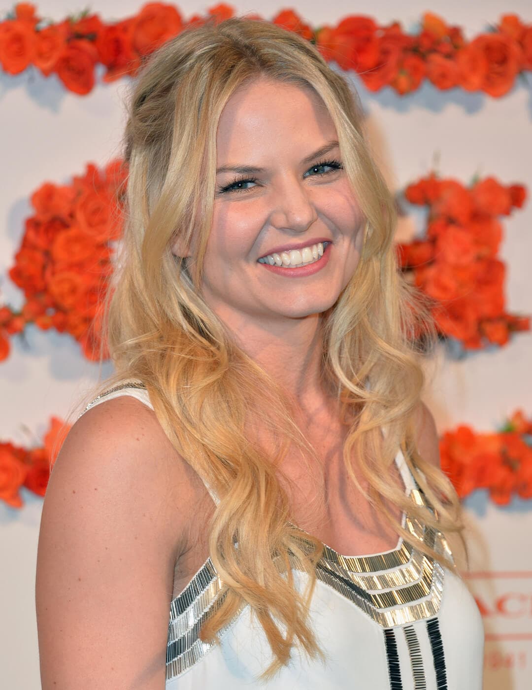 Jennifer Morrison smiling and rocking a half-up waterfall braids hairstyle against a wall of roses