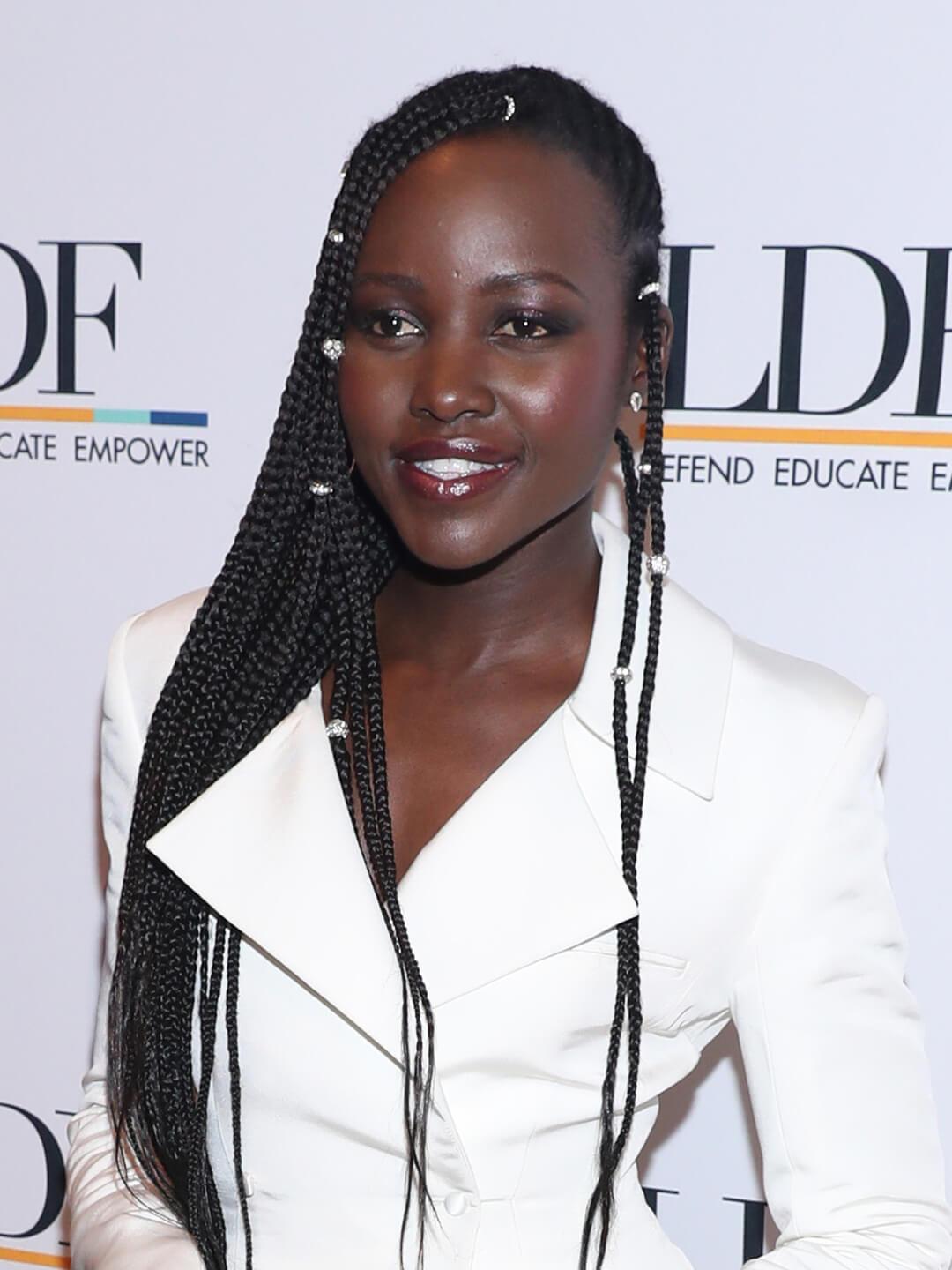 Lupita Nyong'o in a white suit rocking a long, bejeweled goddess braids hairstyle