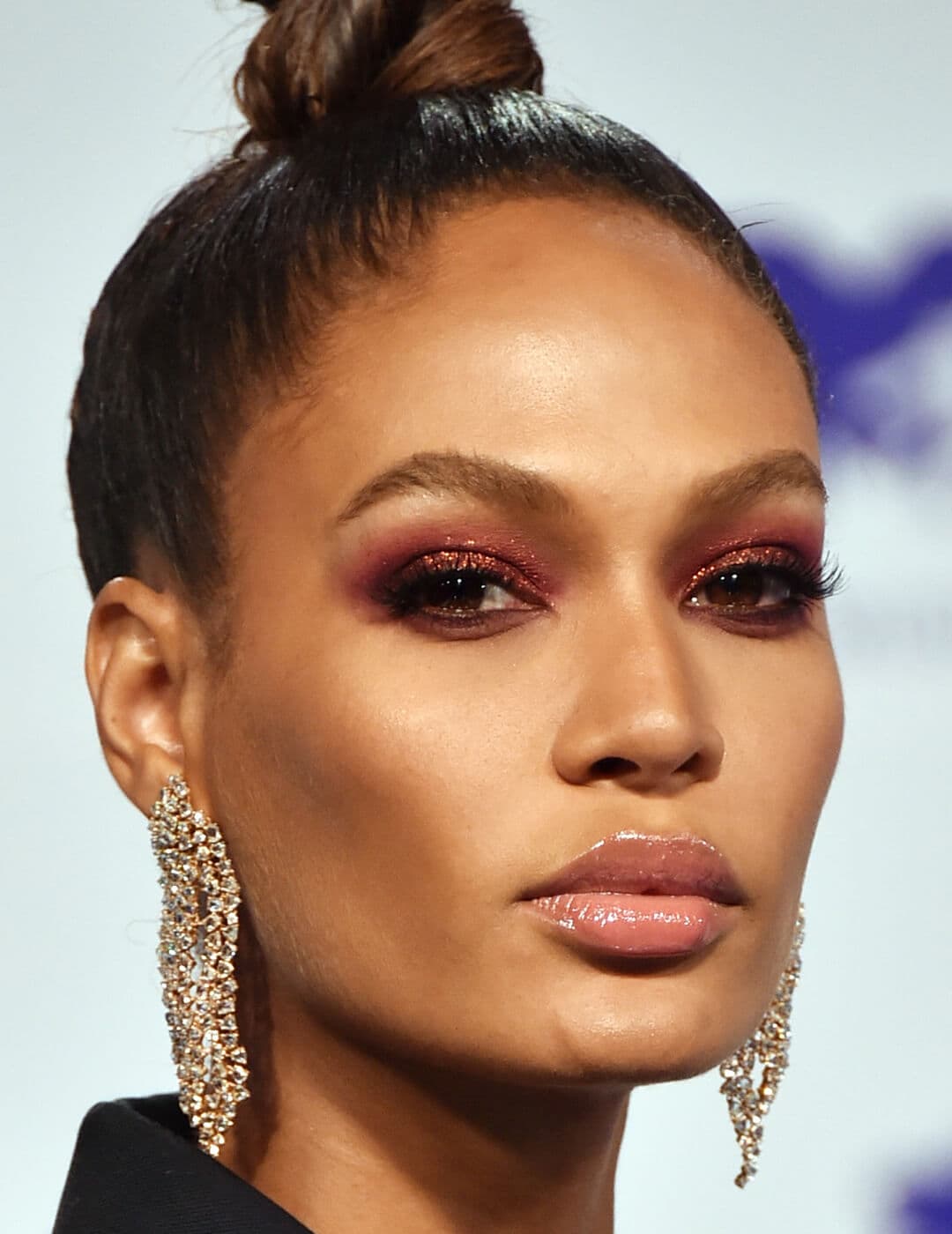 Close-up of Joan Smalls rocking a glittery red smoky eye makeup look, top bun, and gold dangling earrings