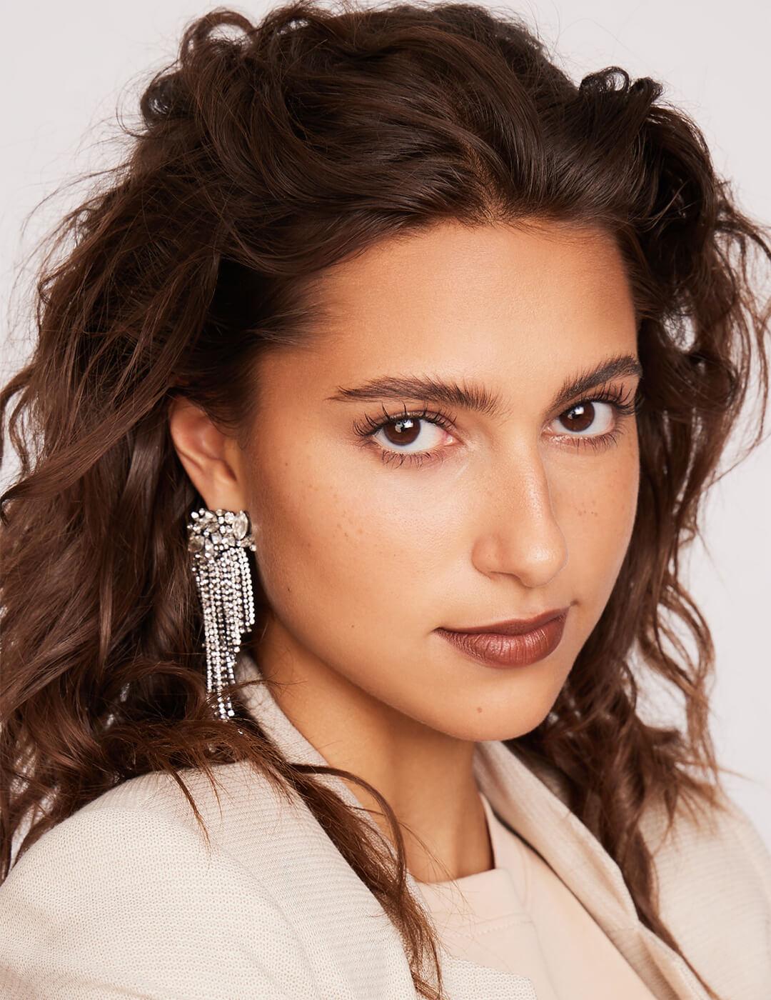 Close-up of a model rocking a wavy side part hairstyle, silver dangling earrings, and a minimal makeup look with brick red lips