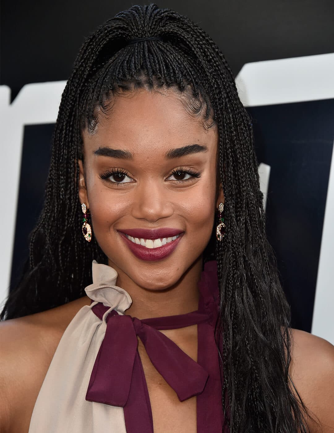 Laura Harrier in a maroon and cream dress and rocking a braided half updo hairstyle
