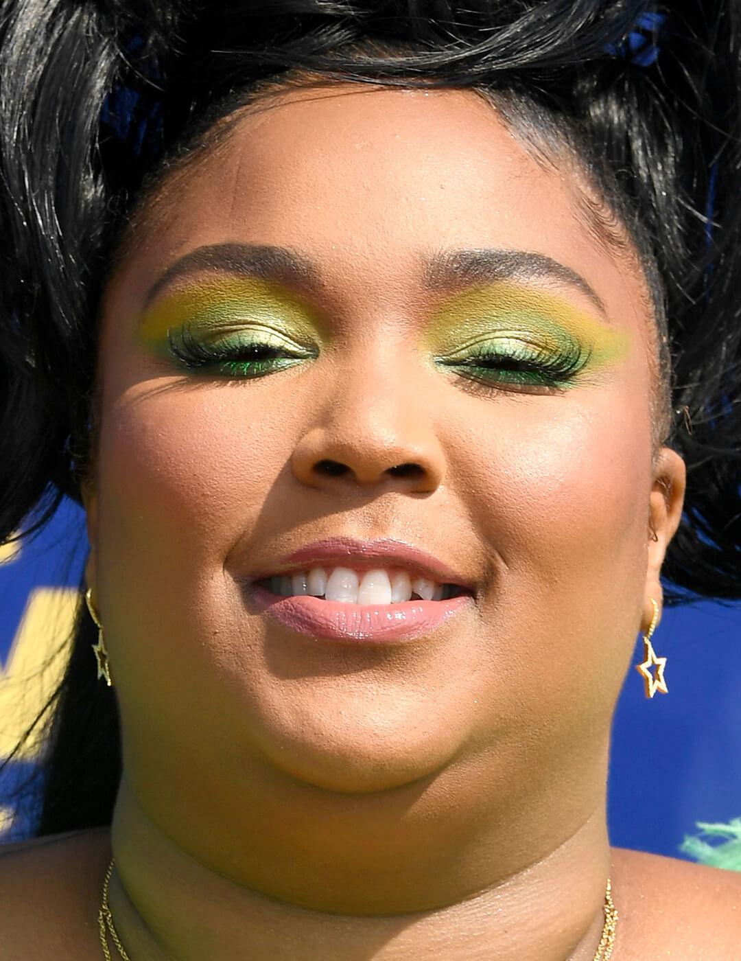 Close-up of a smiling Lizzo rocking a lime green eye makeup look
