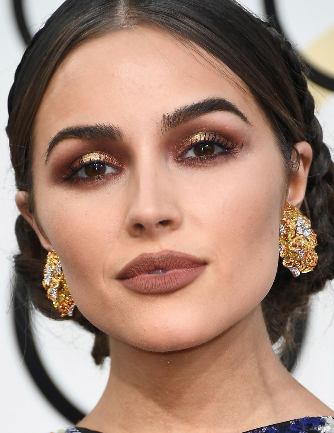 Olivia Culpo rocking a brown and gold eye makeup look, brown lips, and gold earrings