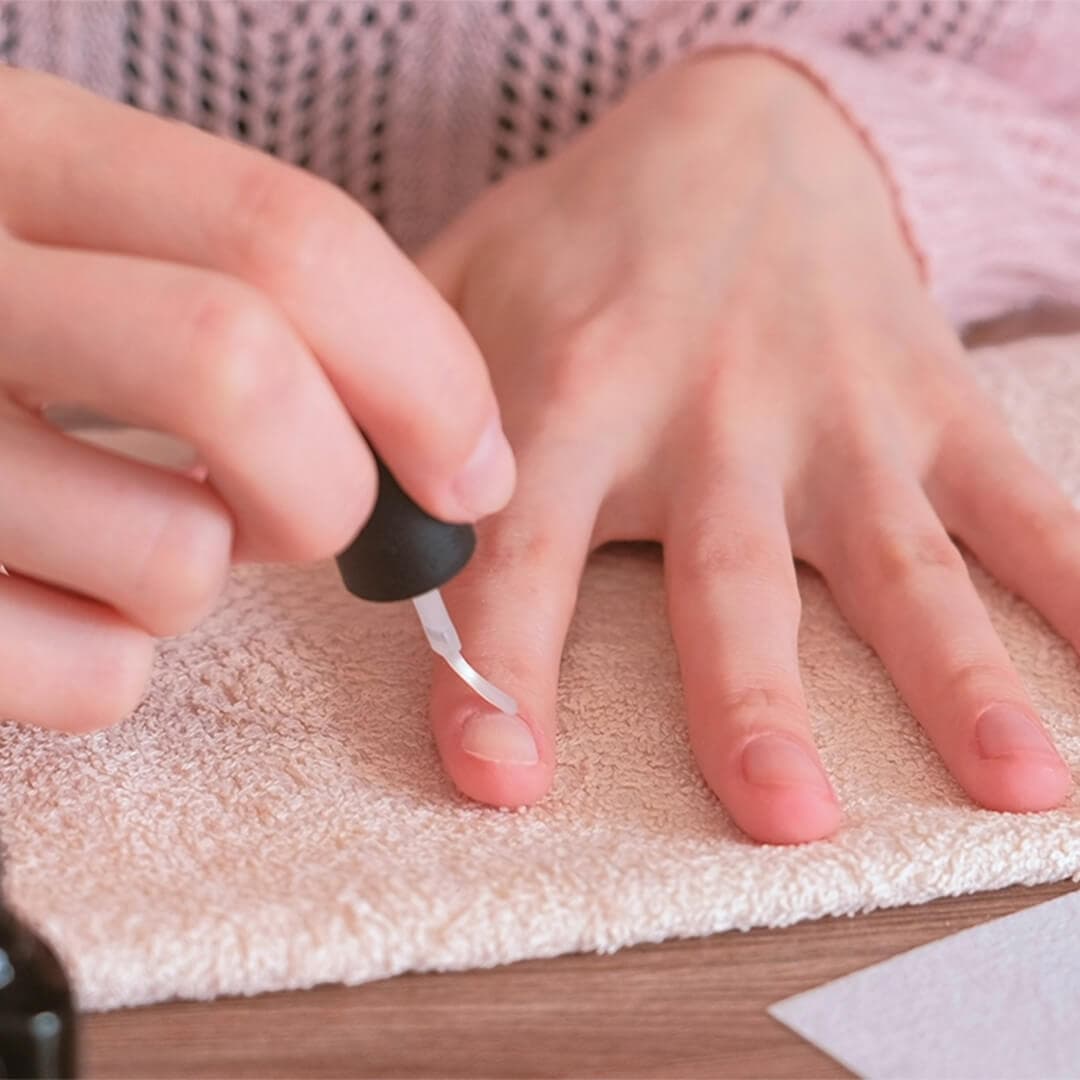 Close-up image of woman's hands putting nail oil on her nail