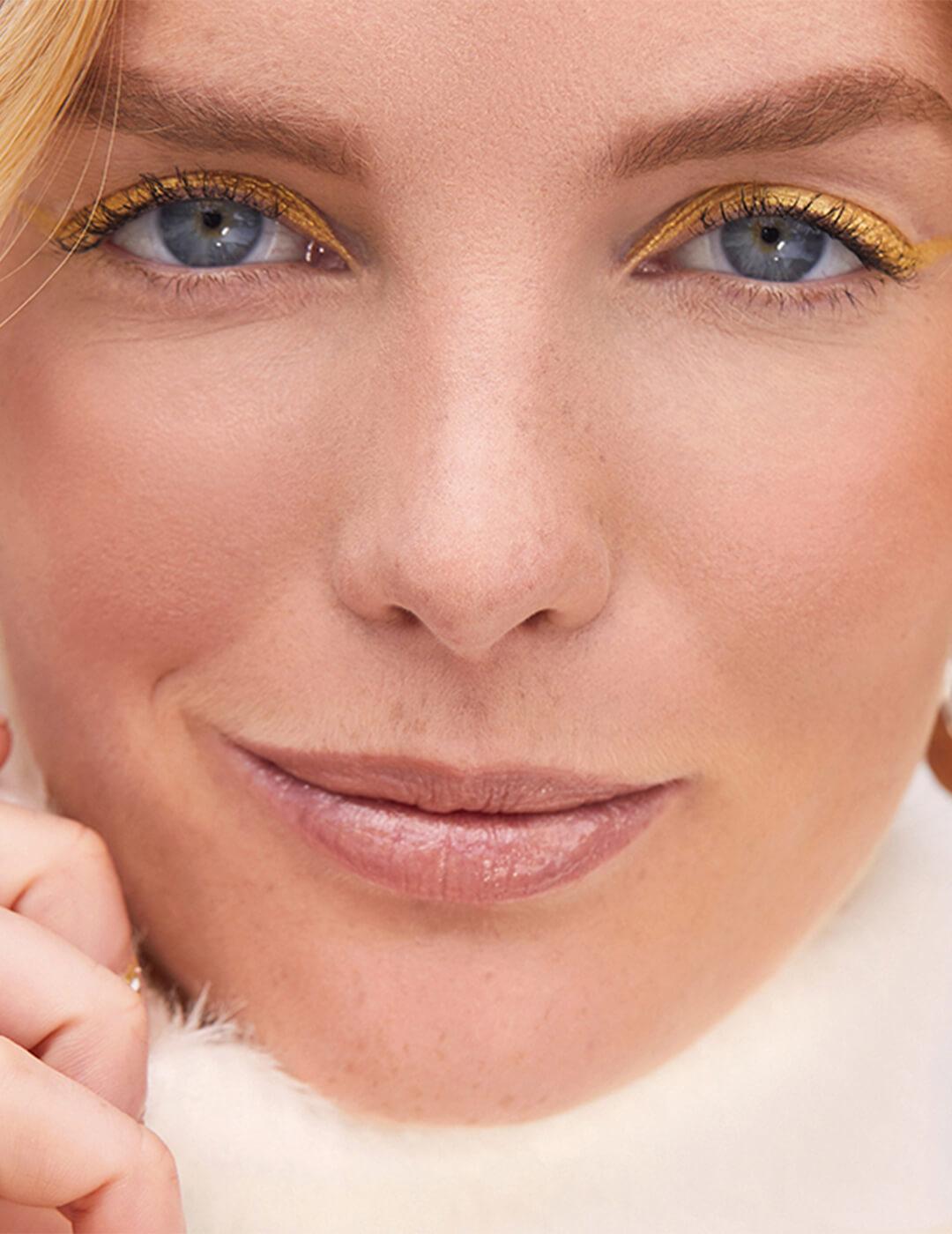 Close-up of a smirking model rocking a gold eyeliner makeup look