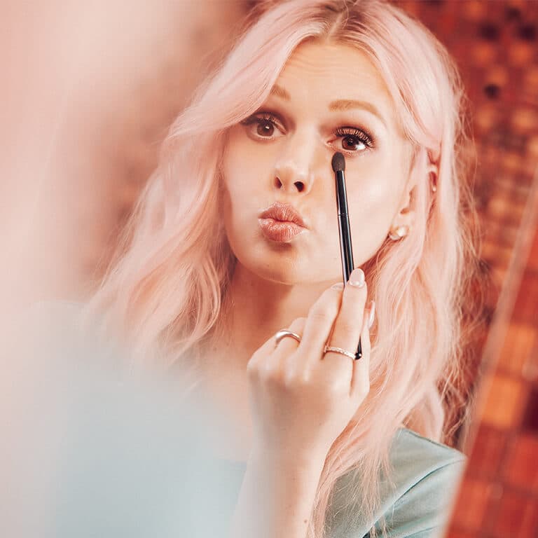 An image of a model applying eyeshadow using a small fluffy brush
