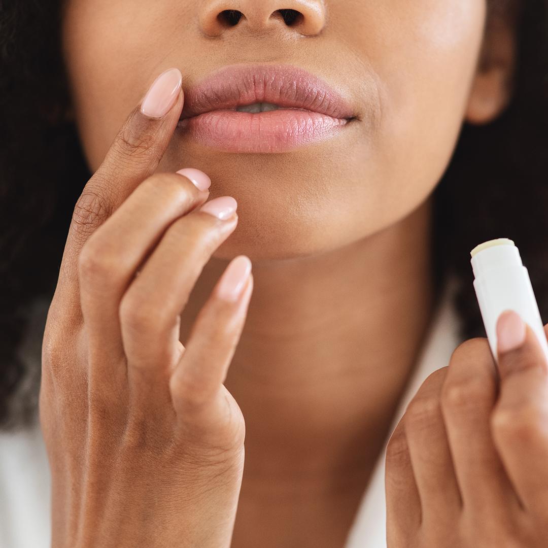 An image of a woman focused on touching the side part of her lips while holding a white lip chapstick