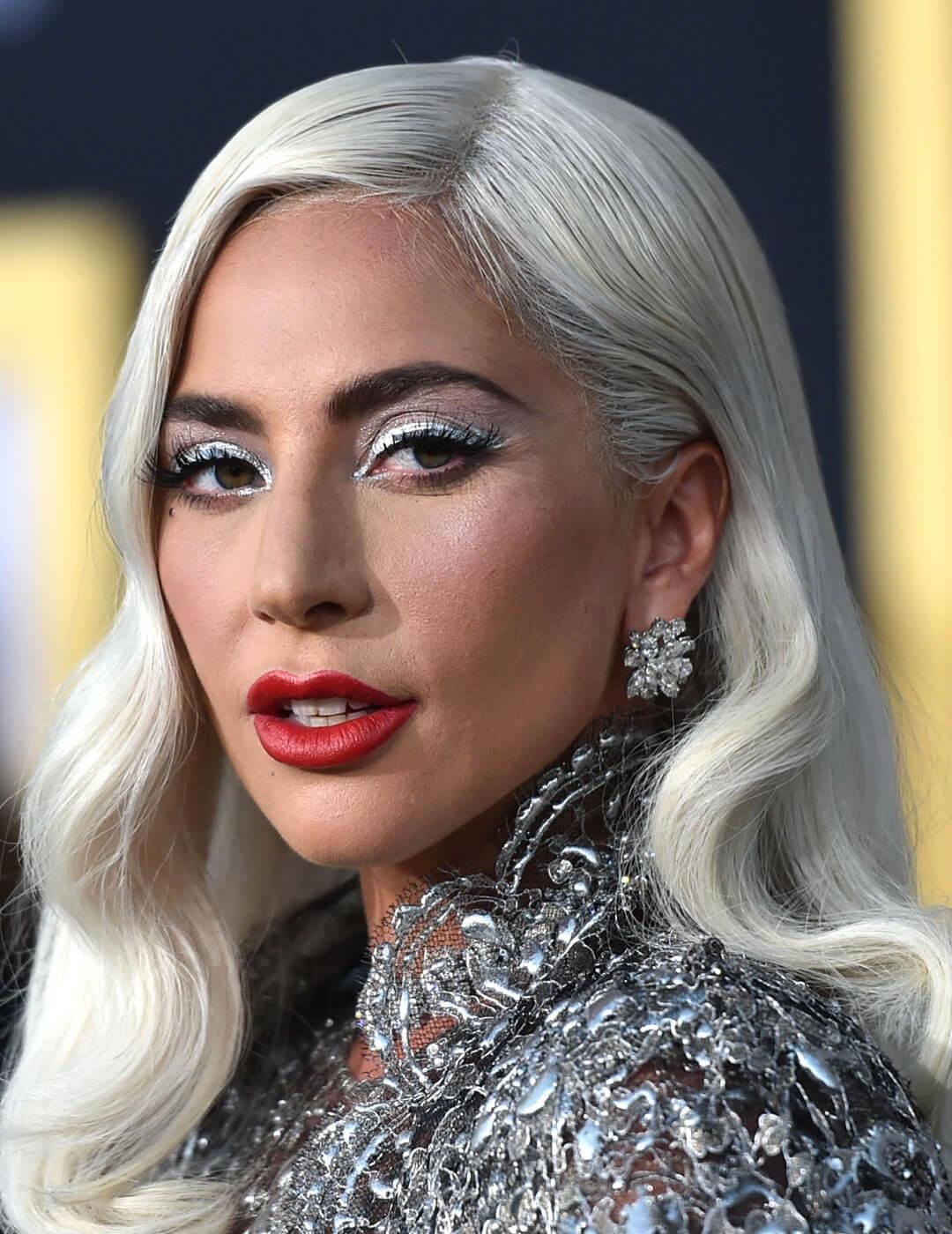 A photo of Lady Gaga with a  platinum blonde hair and silver eyeshadow, dress, and earrings
