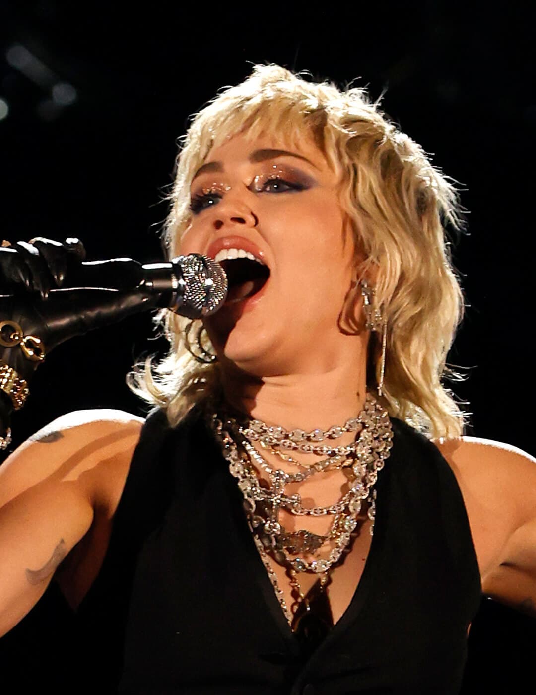 Miley Cyrus in a black outfit and short, wavy hairstyle singing her heart out
