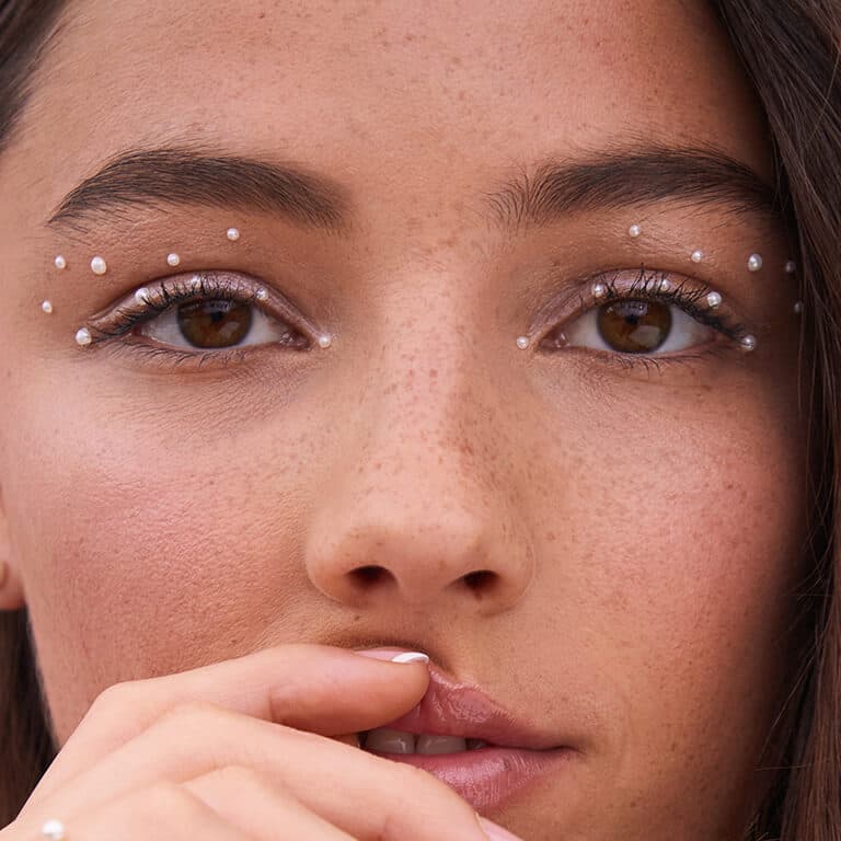 A closeup image of a model rocking a natural rosy eyeshadow look with pearls holding her upper lip