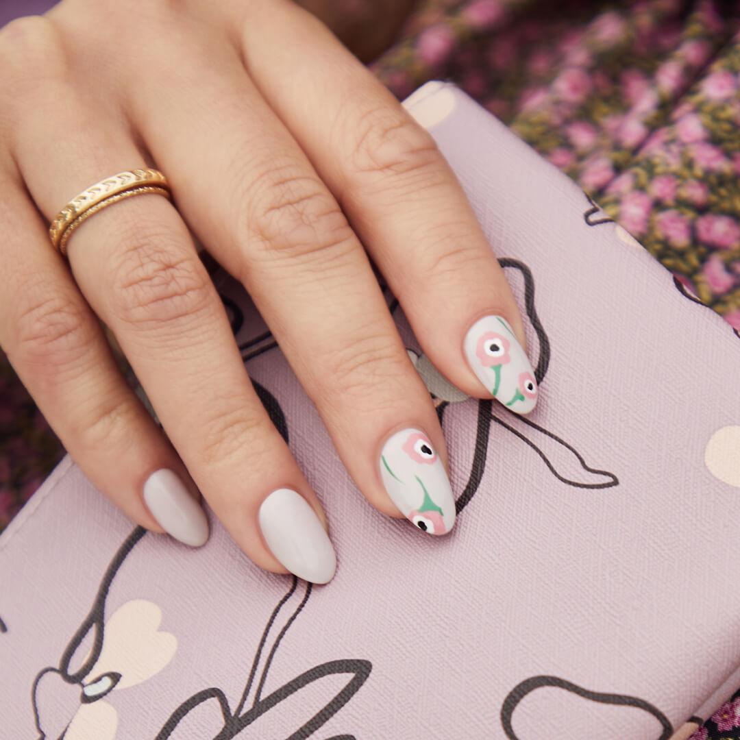 Close-up of a model's hand with light mint blue nail polish and pink floral accents holding the April 2020 IPSY Glam Bag