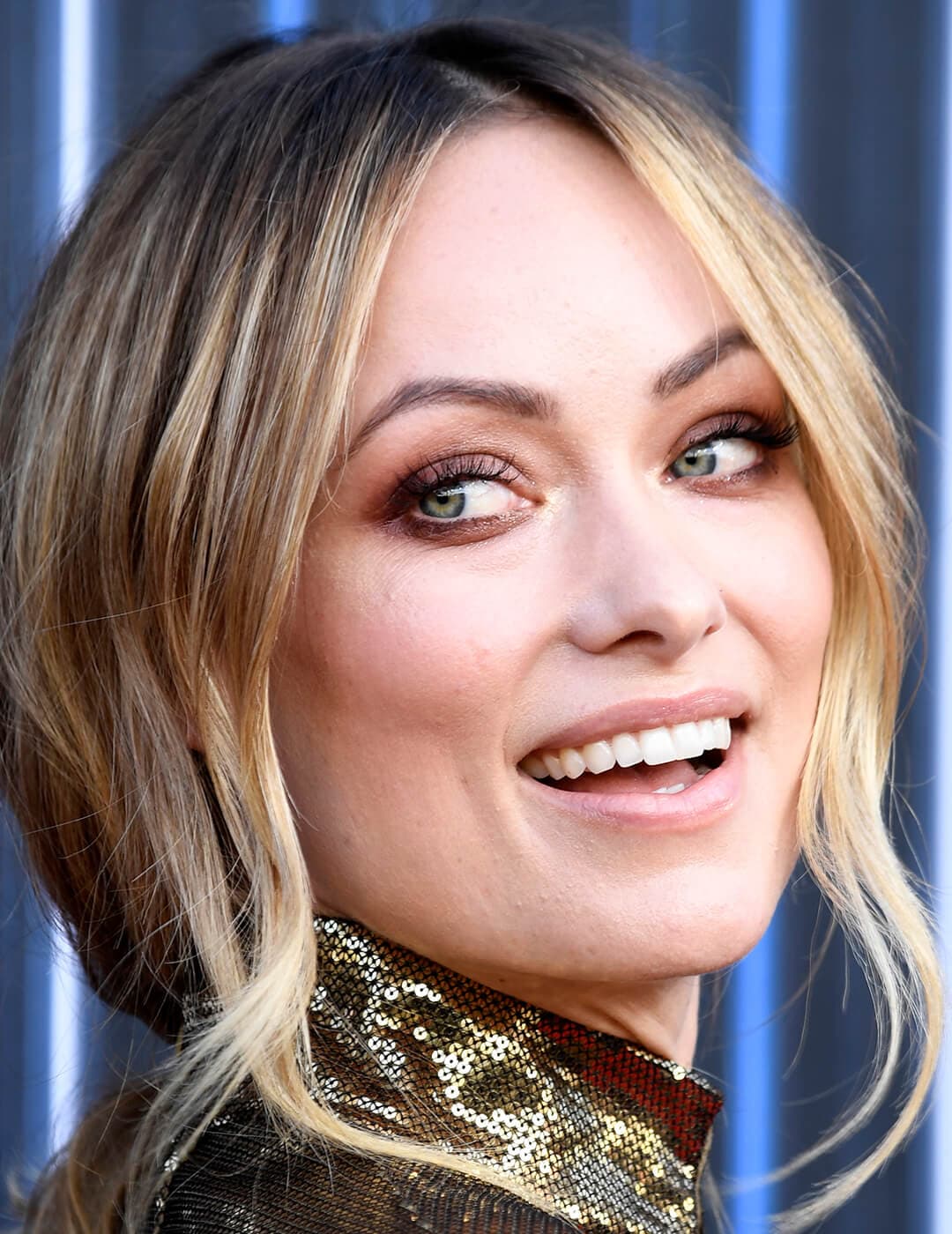 A closeup photo of Olivia Wilde with blonde hair wearing a gold sequin dress