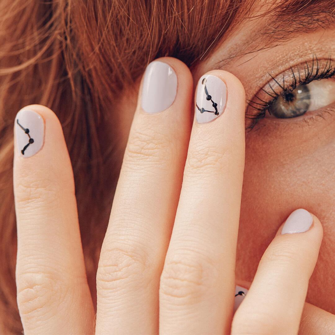 Image of hand with constellation inspired nail art against a woman's face