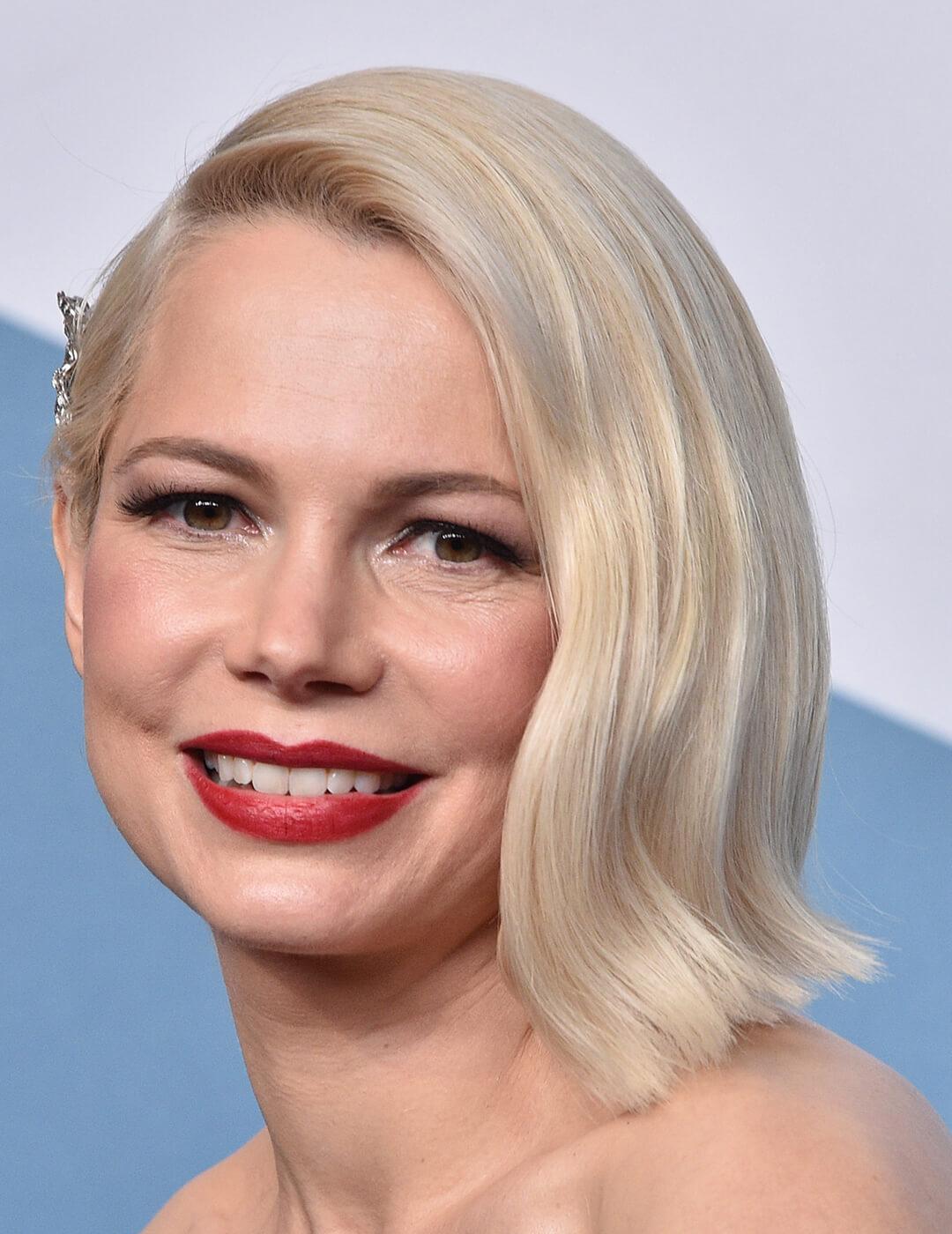 An image of Michelle Williams wearing a bold red lipstick with her hair tucked on the side of her face