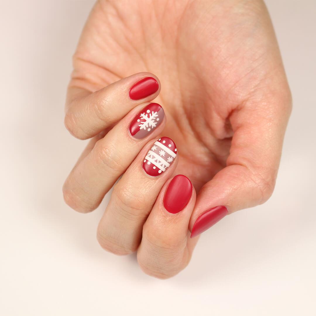 Image of a model's hand with a red and white snowflakes and sweater themed nail art mani