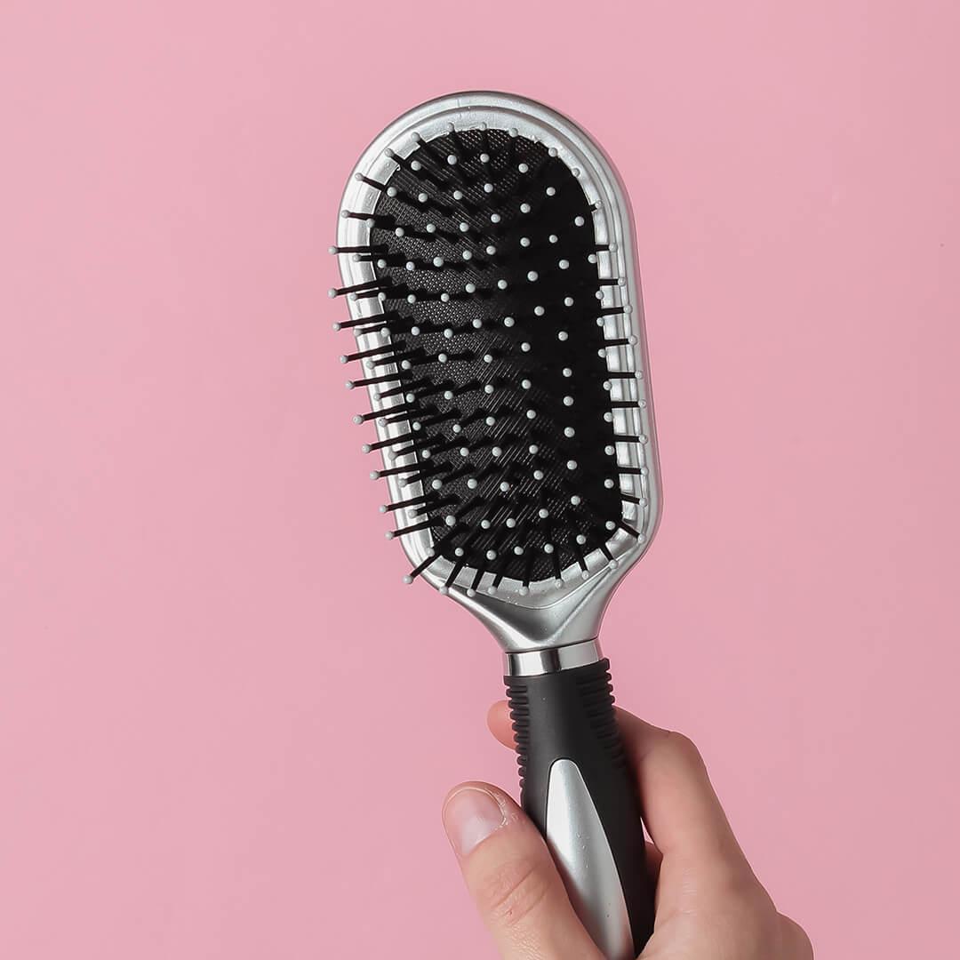 A photo of a mode's hand holding a comb on a pink pastel background