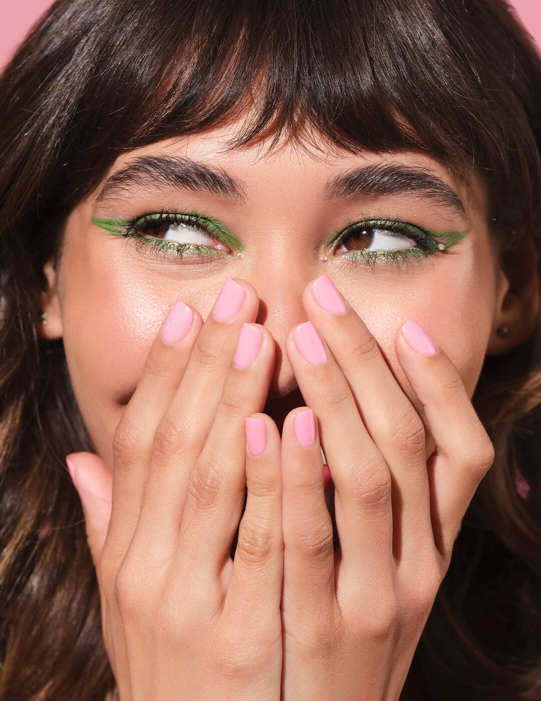 Close-up of a model rocking a bold green eyeliner makeup look and covering half of her face with her hands