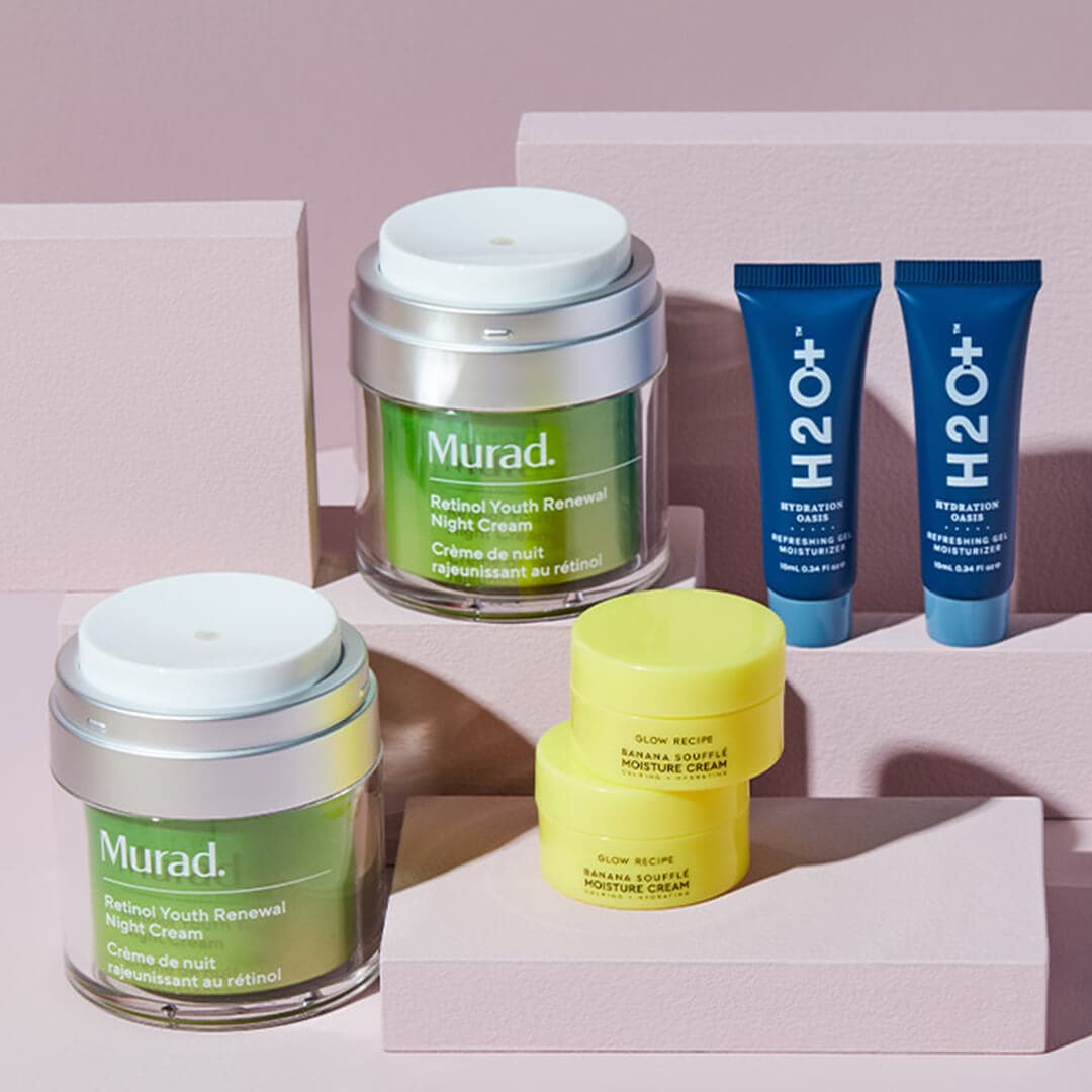 Two jars of MURAD Retinol Youth Renewal Night Cream, two pots of GLOW RECIPE Banana Souffle Moisturizer Cream, and two tubes of H2O+ Hydration Oasis Refreshing Gel Moisturizer on small mauve boxes against mauve background