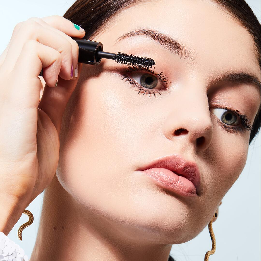 Close-up of a model looking down while applying mascara