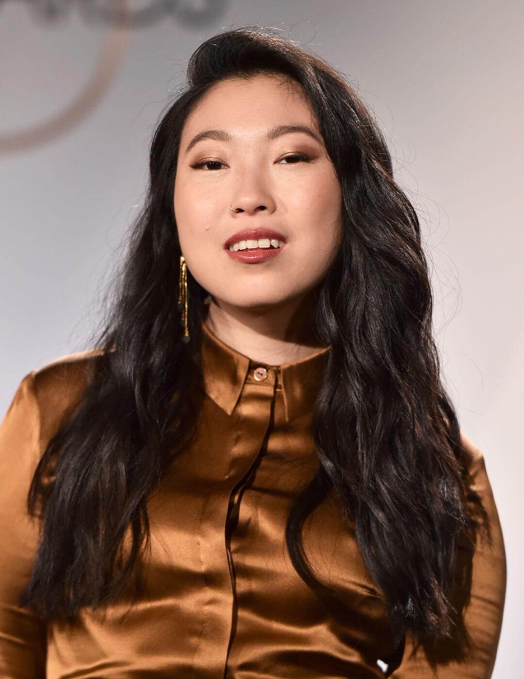 Awkwafina posing in a copper dress and beach waves hairstyle