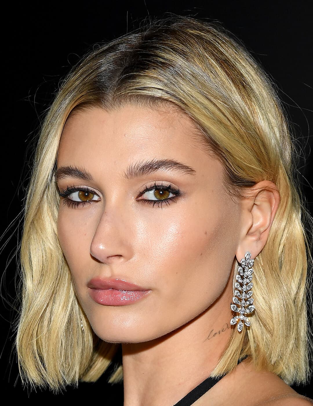 A photo of Hailey Bieber with her hair tucked in her ear showing her dazzling silver earring