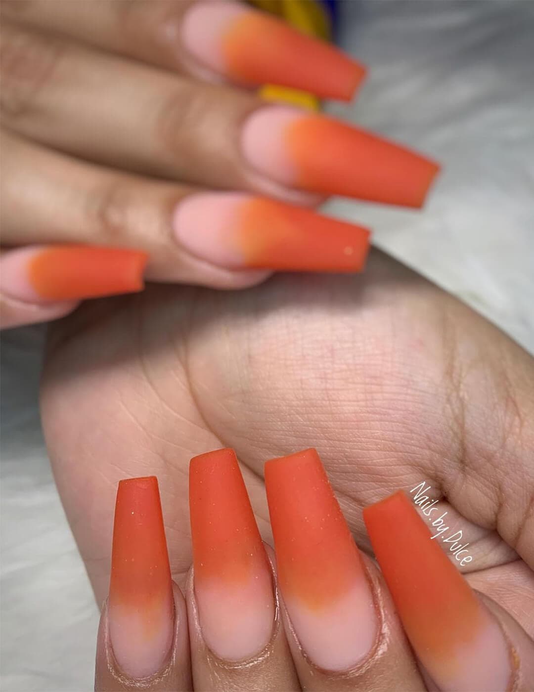 Close-up of a woman's hands with matte orange ombré nail art
