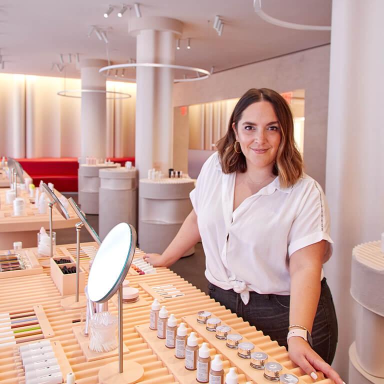 An image of Marta Topran leaning on a desk full of mirrors and beauty products