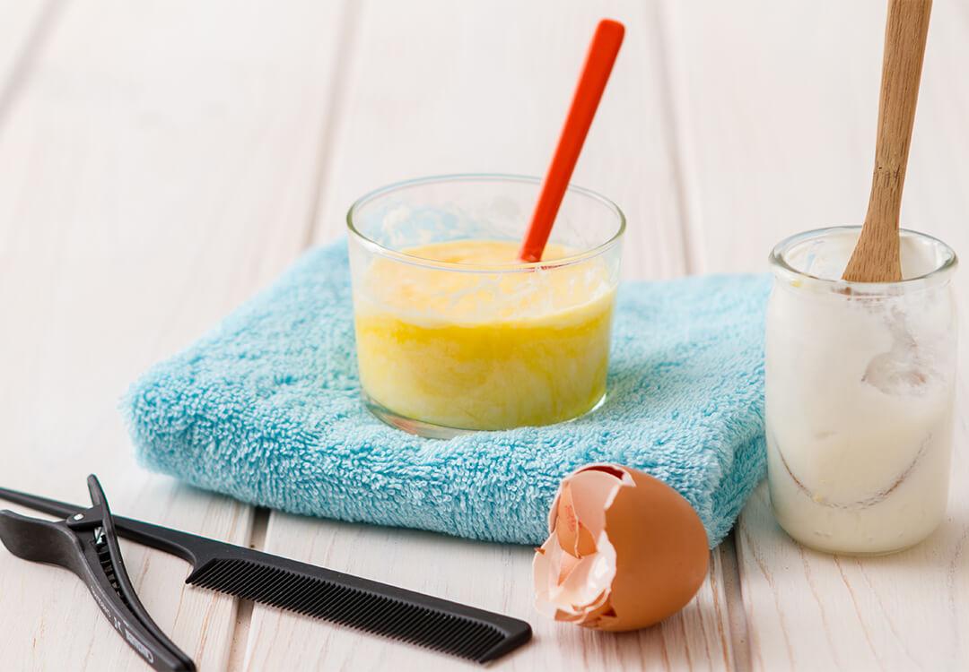Image of glasses with yogurt and egg mask, egg shell, hair clip, and comb on wooden surface