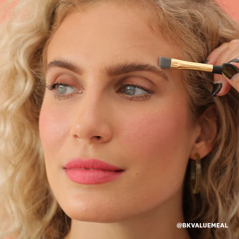 An image of a model blending concealer over her eyebrow with a smudge brush