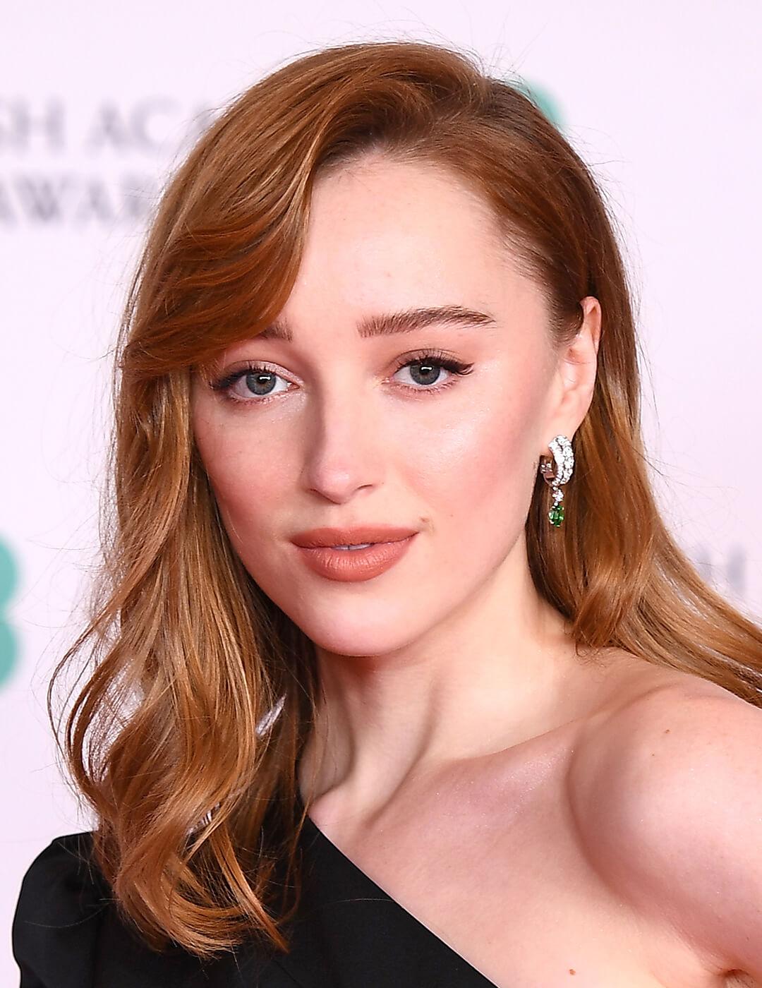 A photo of Phoebe Dynevor with a copper colored hair wearing a black dress