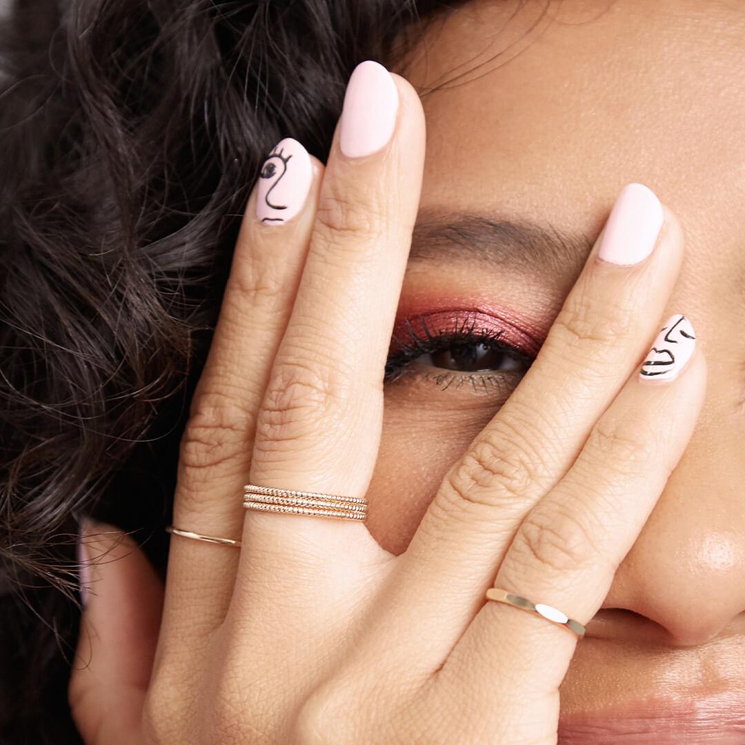 Close-up image of a model peeping through her hand with artsy face silhouette nail art