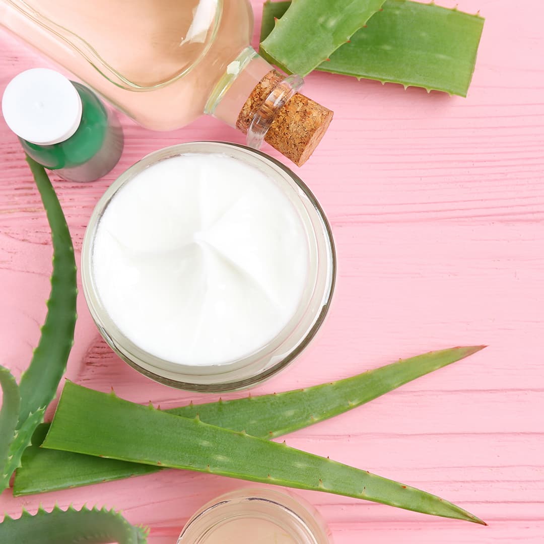 A photo of an aloe vera lotion with aloe vera leaves on a pink wooden background