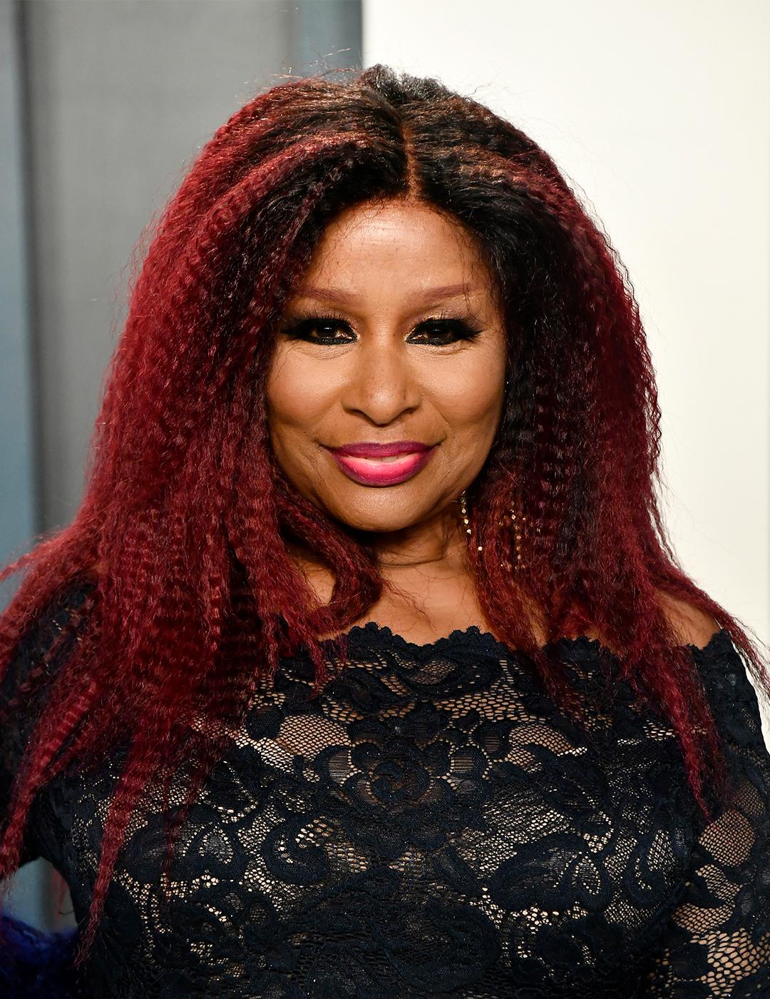 A photo of Chaka Khan wearing a black lace dress with her red colored crimped textured hair