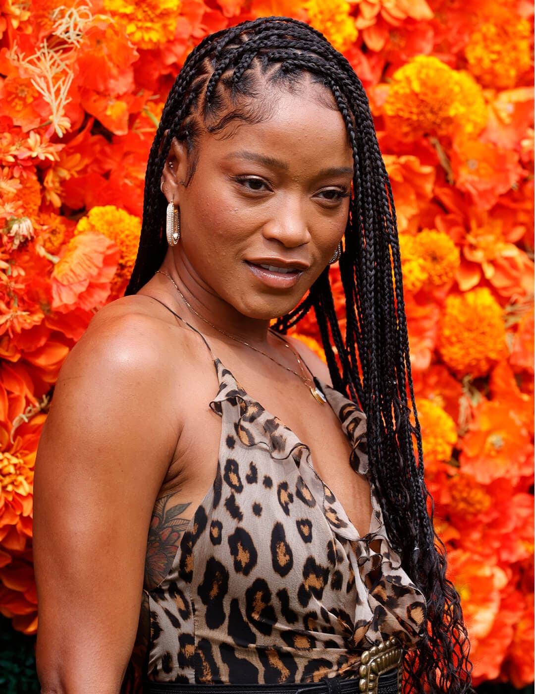 Keke Palmer rocking a side part braided hairstyle and leopard print dress against orange flowers