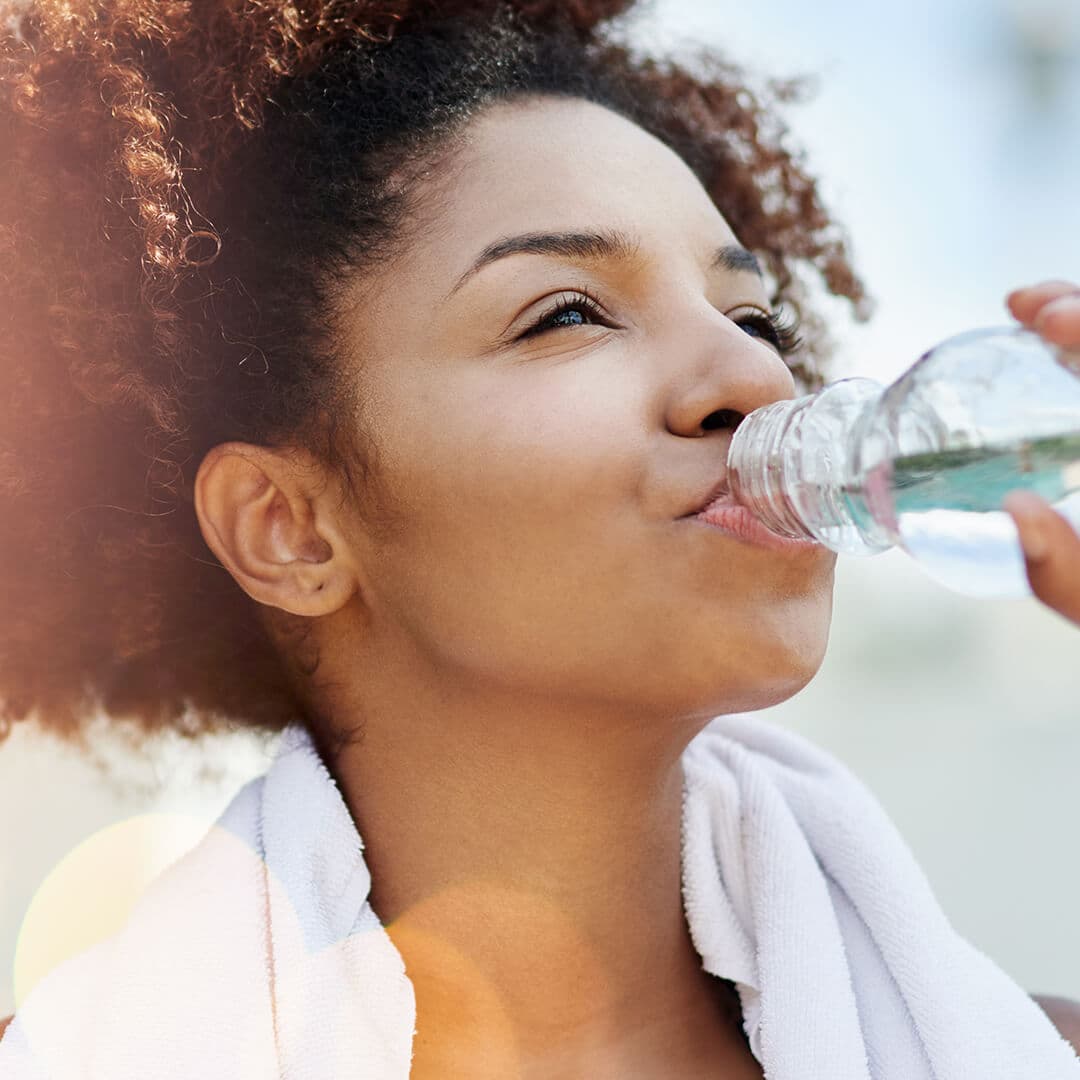 Photo of a woman drinking a bottle of water with a towel on her neck