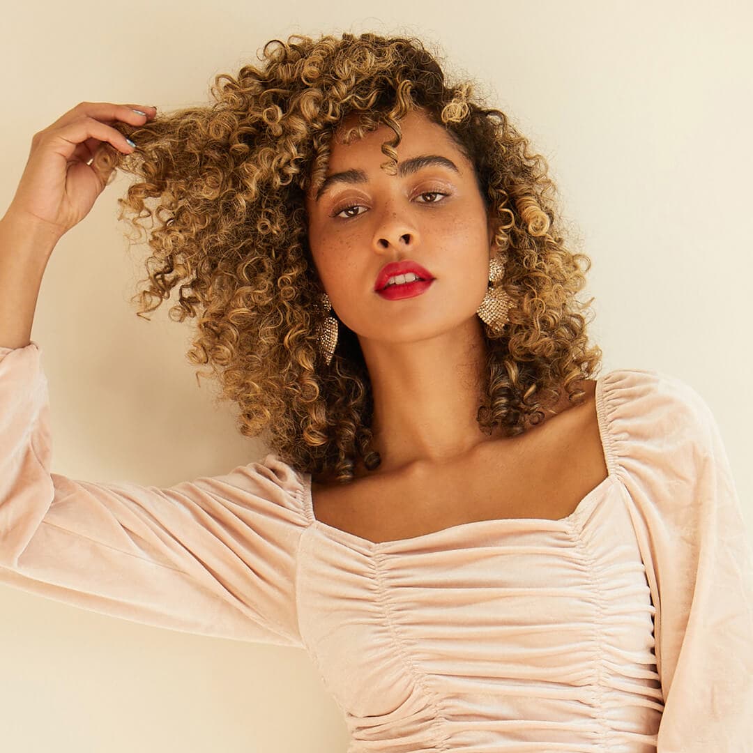 Image of a curly-haired model posing and touching her hair