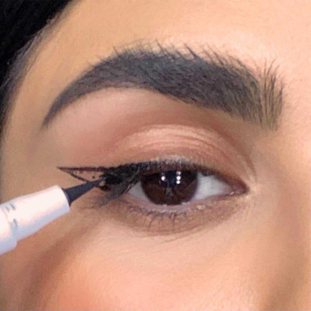 Close-up of a woman filling in her cat eye guide with an eyeliner