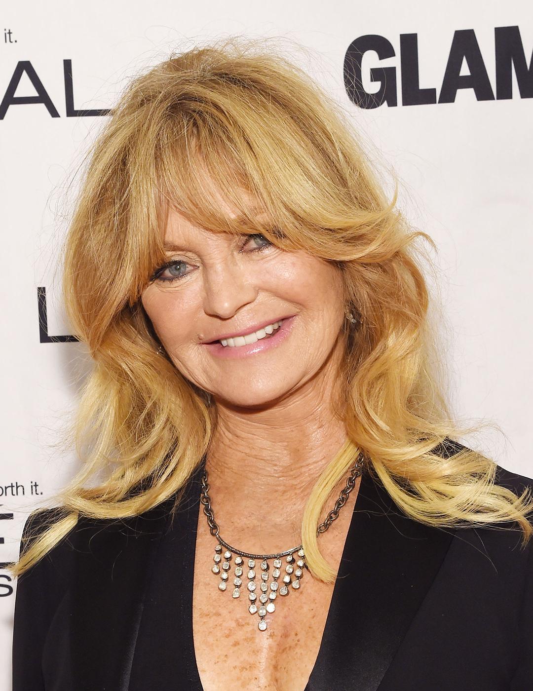A photo of Goldie Hawn wearing a black suite and a chained necklace along with her blond ‘70s-style bangs