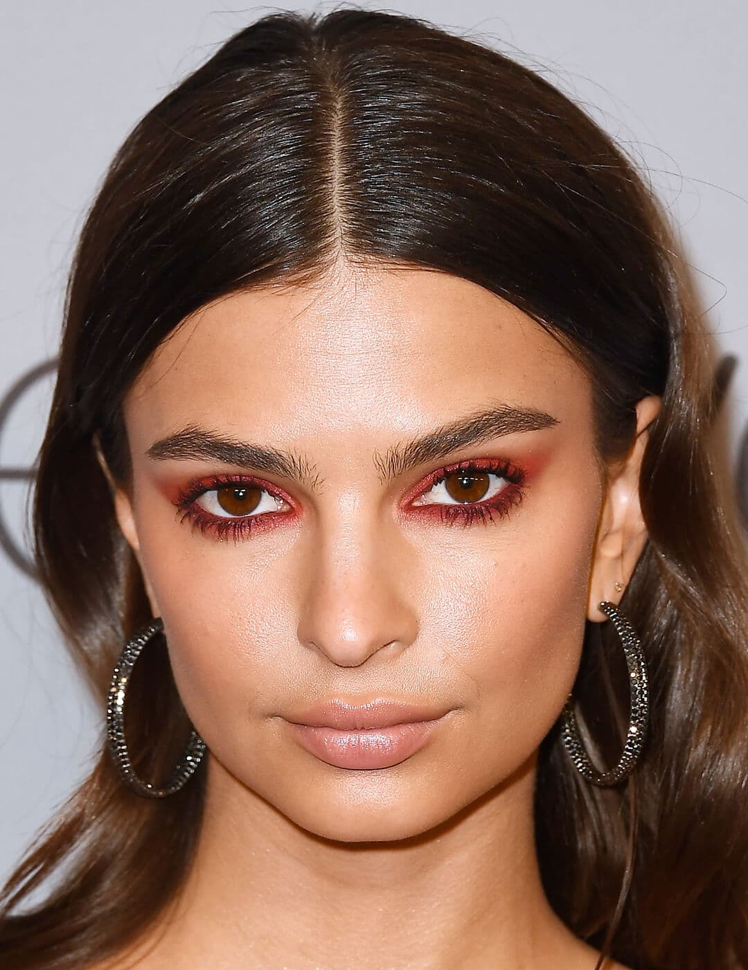 Close-up of Emily Ratajkowski rocking a red eye makeup look and black hoop earrings