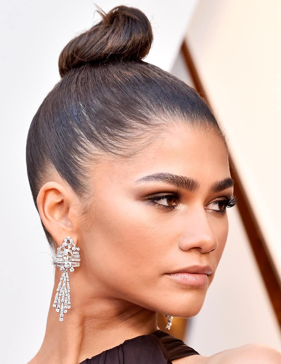 A close-up photo of Zendaya with her sleek and chic top knot hairstyle showing her facial features and silver earring