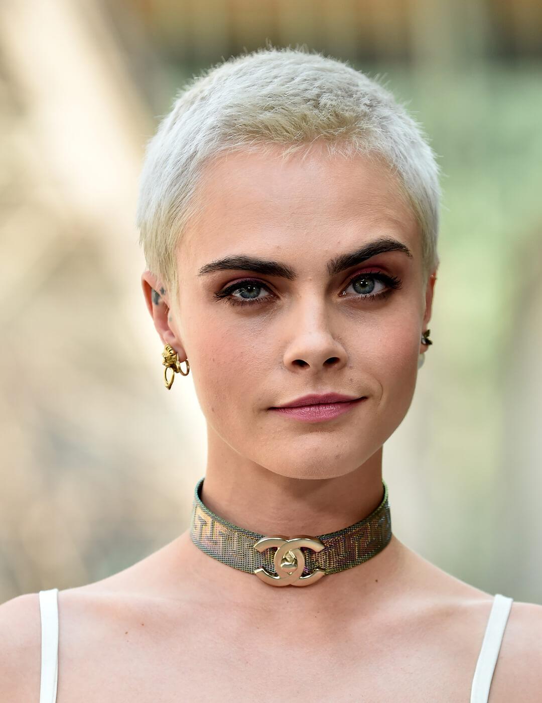 A photo of Cara Delevingne with bleached short cut wearing a white tank top and a Chanel choker