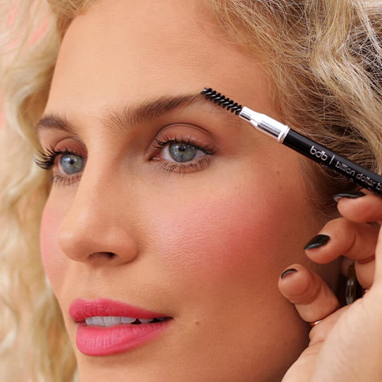 An image of a model brushing up her brows using the BILLION DOLLAR BROWS spoolie.