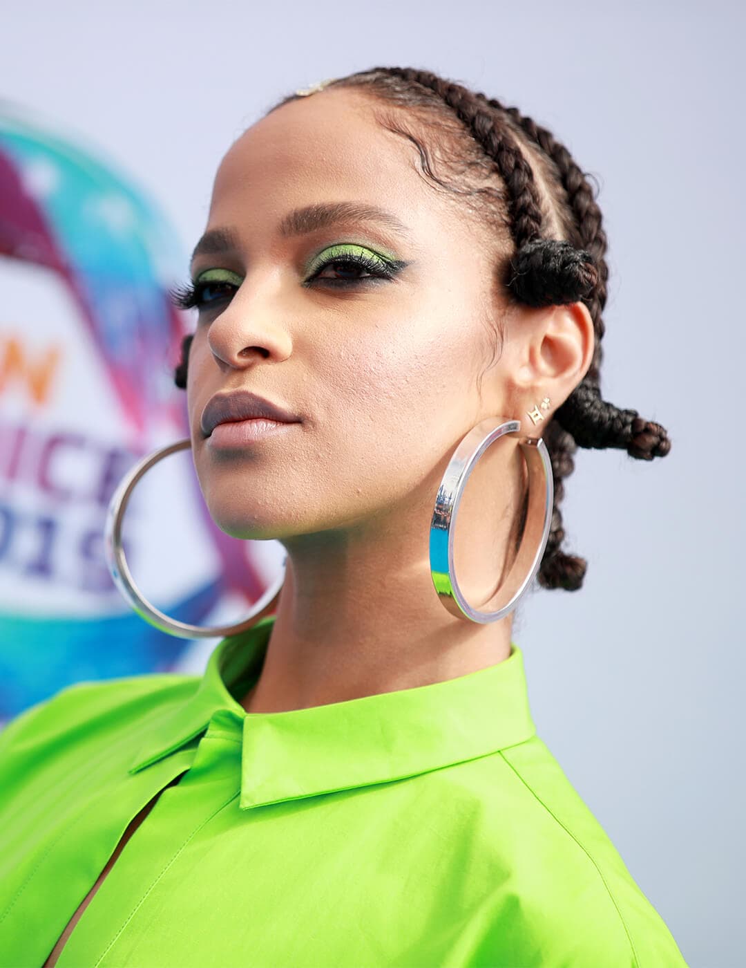 Megalyn Echikunwoke going bold in a neon green shirt, green eyeshadow look, big hoop earrings, and Bantu braids hairstyle