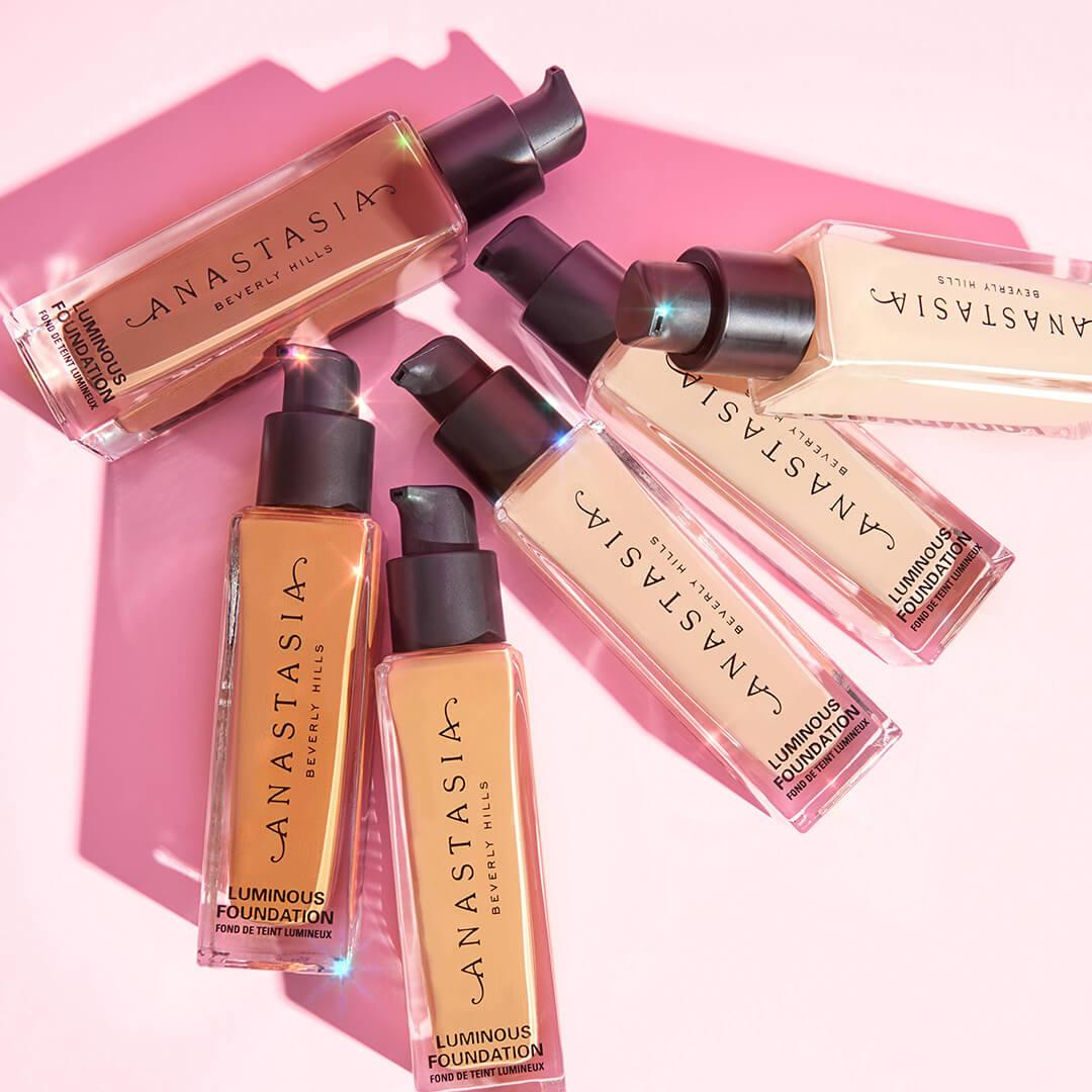 A photo of different shades of ANASTASIA BEVERLY HILLS Luminous Foundation on a pink background