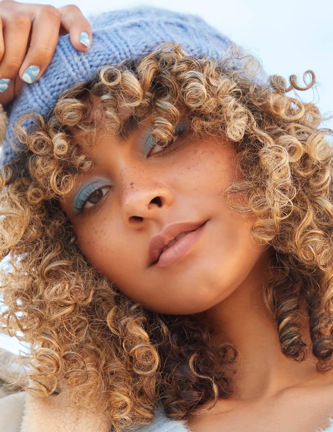 A photo of a blonde curly hair wearing a blue bonnett and eyeshadow
