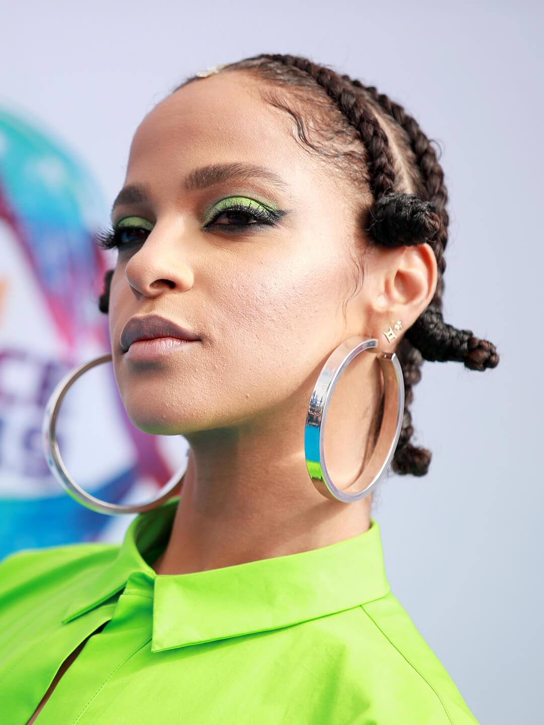 Megalyn Echikunwoke in a neon green outfit rocking a braided space bun hairstyle and big hoop earrings